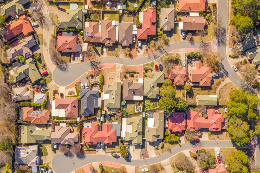 An aerial view of a neighborhood during autumn. Trees with orange and red leaves scattered among houses in a neighborhood.